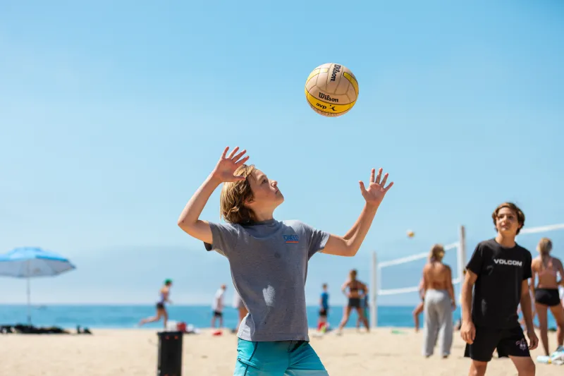 Camper serves a beach volleyball at East Beach