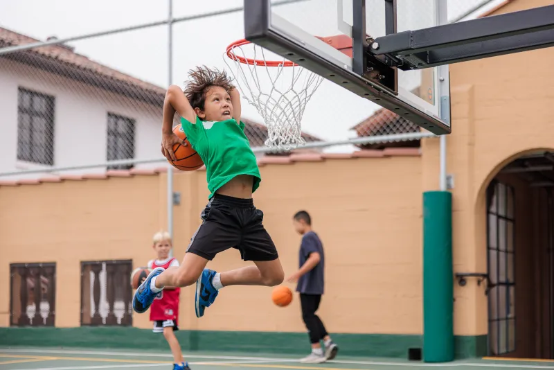 Camper jumps up to dunk on the lowered hoop at Basketball Camp
