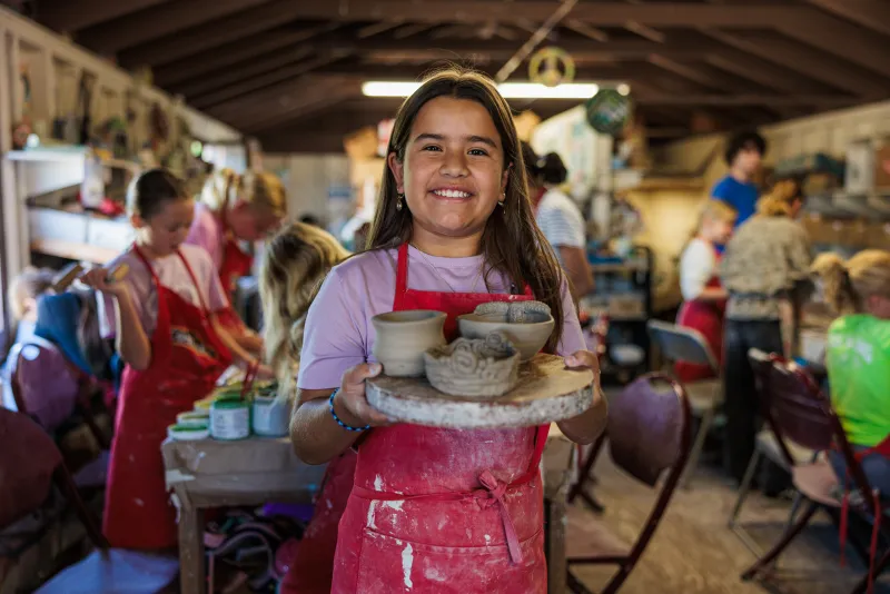 Camper poses with their ceramics displayed at Ceramics Camp