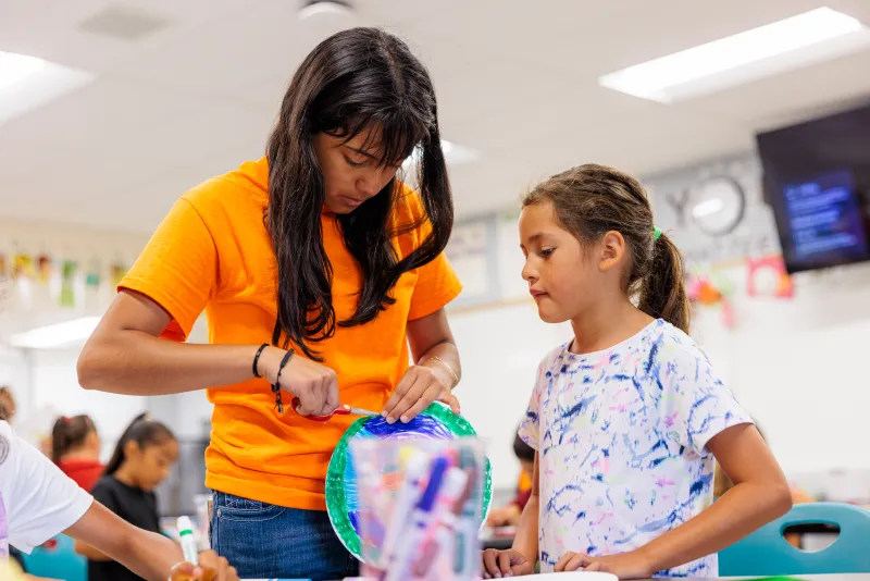 Junior Counselor helps a camper with their arts and crafts project